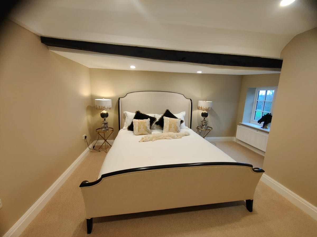 Finished bedroom after decorating, with a bed beneath a dark ceiling beam